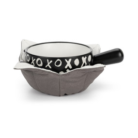 A black ceramic soup crock with a white x and o pattern nestled in a gray fabric cozy with a white polka dot interior.