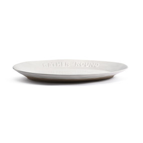 A white ceramic oval platter with a tan textured base. The rim of the platter says "Gather 'Round".