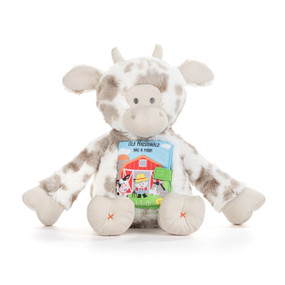 A white and gray plush cow with a fabric storybook attached to its chest titled "Old MacDonald had a farm".