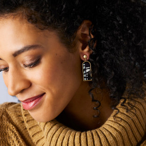 A woman wearing a pair of earrings with a vertical rectangle of black and white geometric artwork.