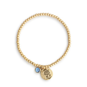 A gold beaded bracelet with a morning glory flower round charm and blue colored stone.