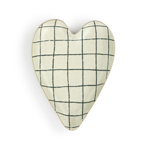A cream heart shaped ceramic spoon rest with dark blue thin plaid lines on it.
