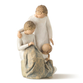 Front view of three figures, all in cream dresses, one seated on rock with quilt over lap, younger child sitting on ground, older woman standing over shoulder