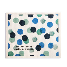 An oversized white biodegradable dish cloth with large green and blue dots and the saying "she who cooks shall not clean".