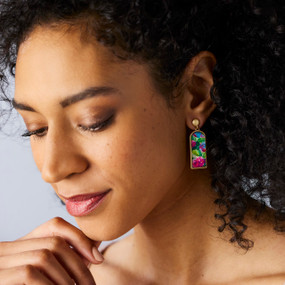 A woman wearing a pair of earrings with pink and blue hydrangea flowers.