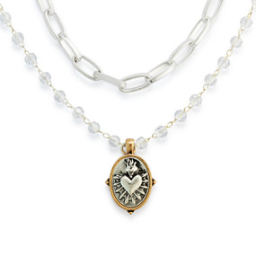 Detail view of the charm on a silver chain and beaded necklace with a silver sacred heart charm with a gold border.