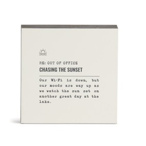 A white square wall art with the saying "RE: Out of Office Chasing the Sunset" with a short write up about someone watching the sunset at the lake.