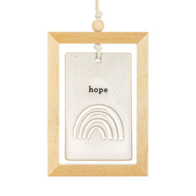 A hanging cream ceramic plaque with a rainbow and the word "hope" suspended inside a light wood open frame.