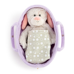 A cream and pink plush puppy inside a purple fabric carrier covered with a gray blanket.