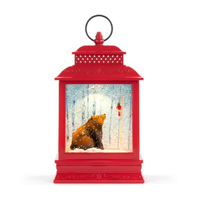 A red lit musical lantern with the image of a bear looking at a cardinal in a tree on the inside.