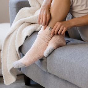 A woman sitting on a gray couch wearing a pair of rose colored socks.