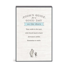 A wall art with an illustration of Pooh and Piglet with a message about Pooh's guide for a good day on the shore.