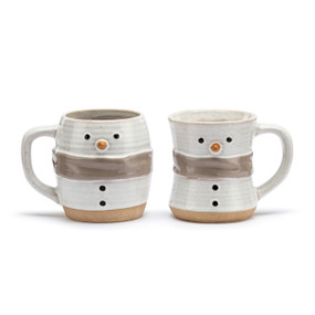 A pair of cream ceramic cuddle mugs that look like snowmen with scarves, one that curves inward and the other curves outward.