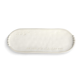 A long cream ceramic platter that says "For Unto Us A Child Is Born" at the bottom with decorative elements on the ends.