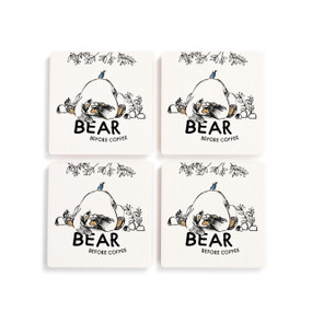 A set of four white square coasters with an illustration of a tired bear and the saying "Bear before coffee".
