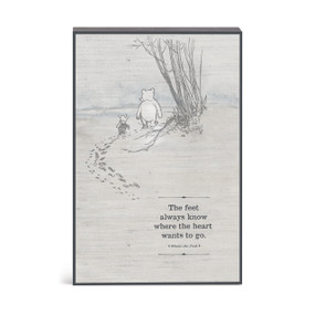A gray wall art with an illustration of Pooh and Piglet walking and the saying "The feet always know where the heart wants to go".