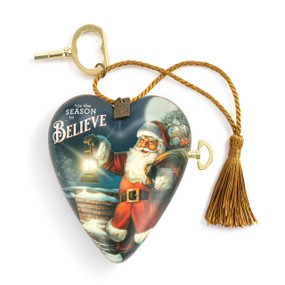 A heart shaped musical sculpture with an image of a traditional Santa and the saying "'tis the Season to Believe". The heart has a gold tassel and gold key attached.