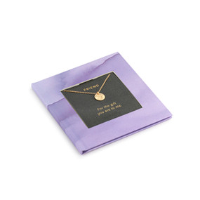 A small square purple book with inspirational content about friendship. There is a gold chain necklace inside with a round charm.