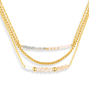 A layered gold necklace made of three different chains with cream beads on them.