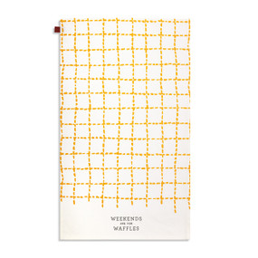 A white and orange plaid kitchen towel with the saying "Weekends are for Waffles" displayed with the towel laid out flat.