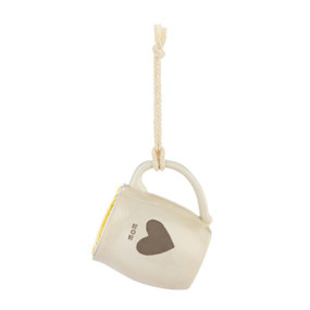 A cream ceramic mini mug that says "mom" with the image of a heart on the front, shown hanging with a coffee pod inside.