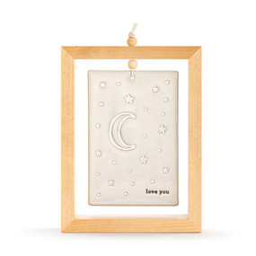 A cream ceramic plaque with the moon and stars and the saying "love you" suspended inside a light wood open frame.