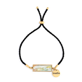An adjustable black string bracelet with a horizontal gold charm with pastel abstract artwork inspired by ArtLifting artist Alene Sirott-Cope. The bracelet also has a small round gold token that says "breathe".