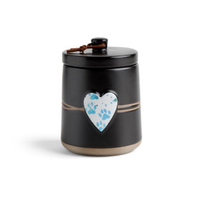 A round black ceramic poured candle with a tan textured base, a lid and a white raised heart on the front with a blue paw print illustration.