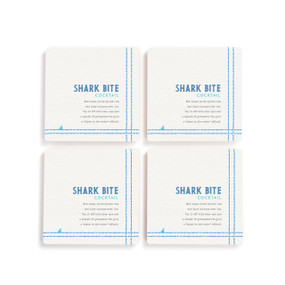 A set of four white square coasters with a basic recipe for a Shark Bite Cocktail written in blue.