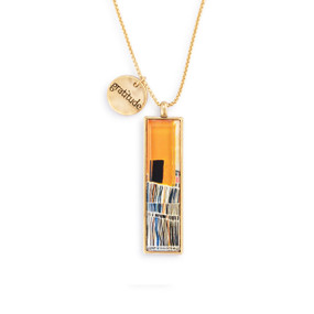 An adjustable gold chain necklace with a vertical gold charm with orange and brown abstract pattern artwork inspired by ArtLifting artist Cheryl Kinderknecht. The necklace also has a small round gold token that says "gratitude".