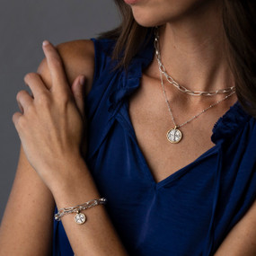 Close up of a woman in a blue blouse wearing a silver necklace and bracelet that have a silver cross medallion.