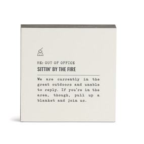 A white square wall art with the saying "RE: Out of Office Sittin' by the Fire" with a short write up about someone in the great outdoors.
