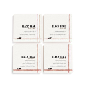 A set of four white square coasters with a basic recipe for a Black Bear Cocktail written in black.