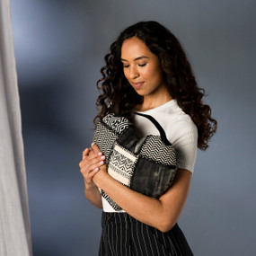 A woman hugging a heart shaped black and cream patchwork pillow with a black handle attached.