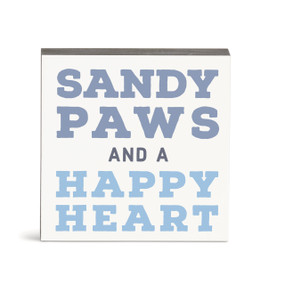 A small square white wall art with the saying "Sandy paws and a happy heart".