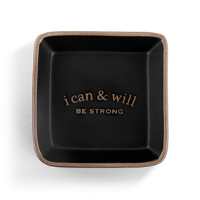 A square black ceramic trinket dish with a tan textured rim that says "i can & will Be Strong" on the inside.