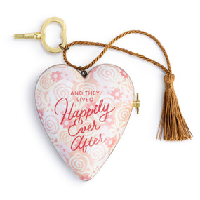 A heart shaped musical sculpture in a white and pink floral pattern that reads "And They Lived Happily Ever After". The heart has a bronze tassel and gold key attached.