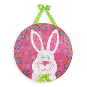 A circular metal door hanger with a white bunny in the center and a pink floral background. The bunny is hanging from a green polka dot ribbon.