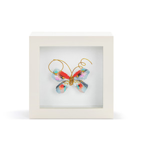 A red and blue butterfly with gold wire tentacles in a white shadow box.