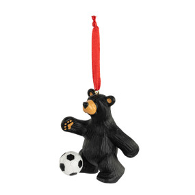 An ornament of a black bear playing with a soccer ball. The ornament has a red ribbon hanger.