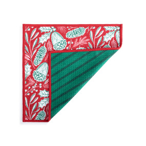 A double sided square dish cloth that is red with pinecone illustrations on one side and green stripe on the other displayed with the green corner turned back.