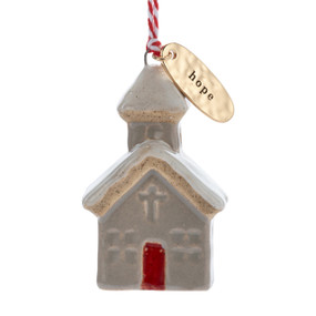 A small ceramic tan church shaped ornament with snow on the roof and a gold metal tag at the top with the word "hope".