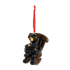 An ornament of a black bear holding a baby bear while sitting in a rocking chair. The ornament has a red ribbon hanger.