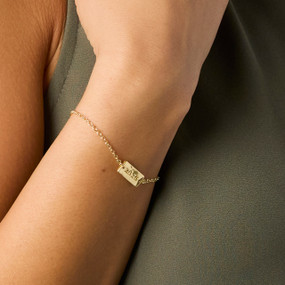A woman wears an adjustable gold chain bracelet with a rectangular gold charm with "XOXO" on it