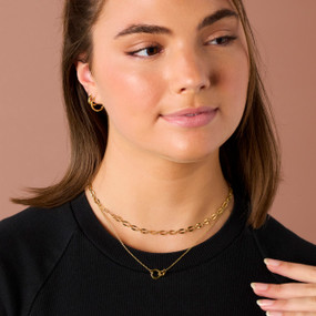 A woman wearing a gold chain necklace and small gold hoop earrings.