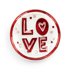 A mini round glass plate with the saying "Love" in red and pink with a red rim.