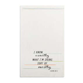 A white kitchen towel with the saying "I know exactly what I'm doing sort of mostly" displayed laid out flat.