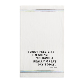A white kitchen towel with the saying "I just feel like I'm going to have a really great day today" displayed laid out flat.