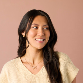 A smiling woman wearing a gold chain necklace with an open gold wire butterfly charm.