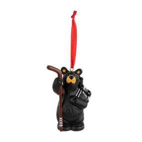 An ornament of a black bear standing with a pair of skates, hockey puck and stick. The ornament has a red ribbon hanger.